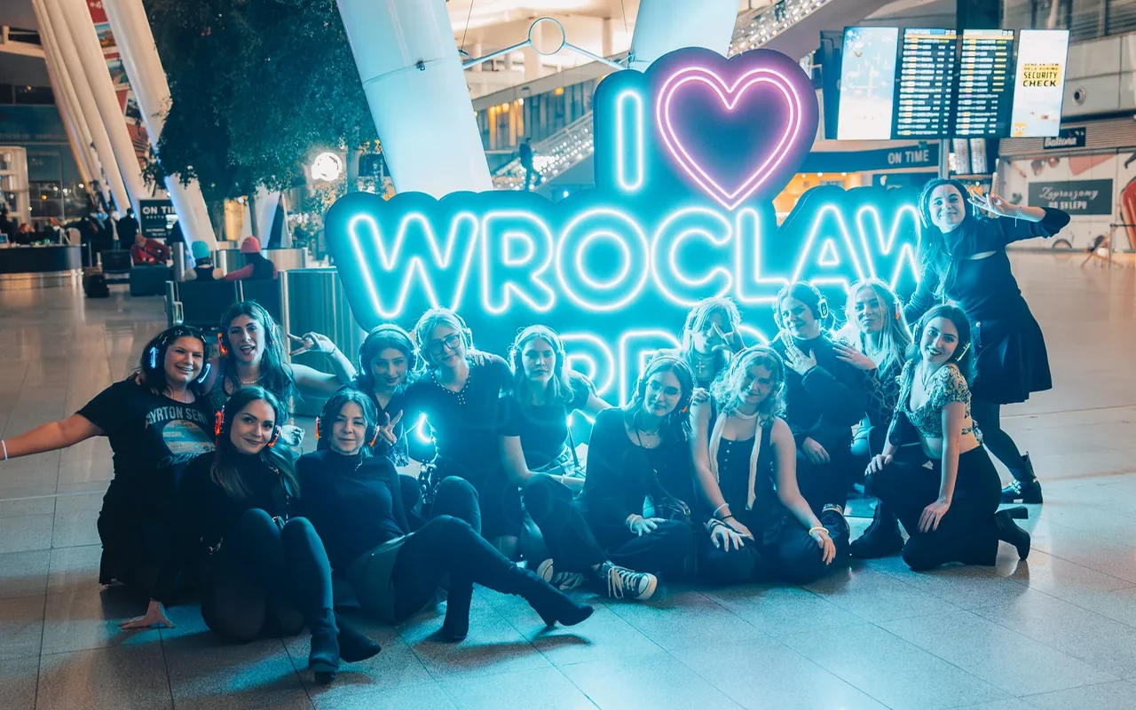 Uczestnicy zebrani przy napisie Wrocław we wnętrzu terminala
